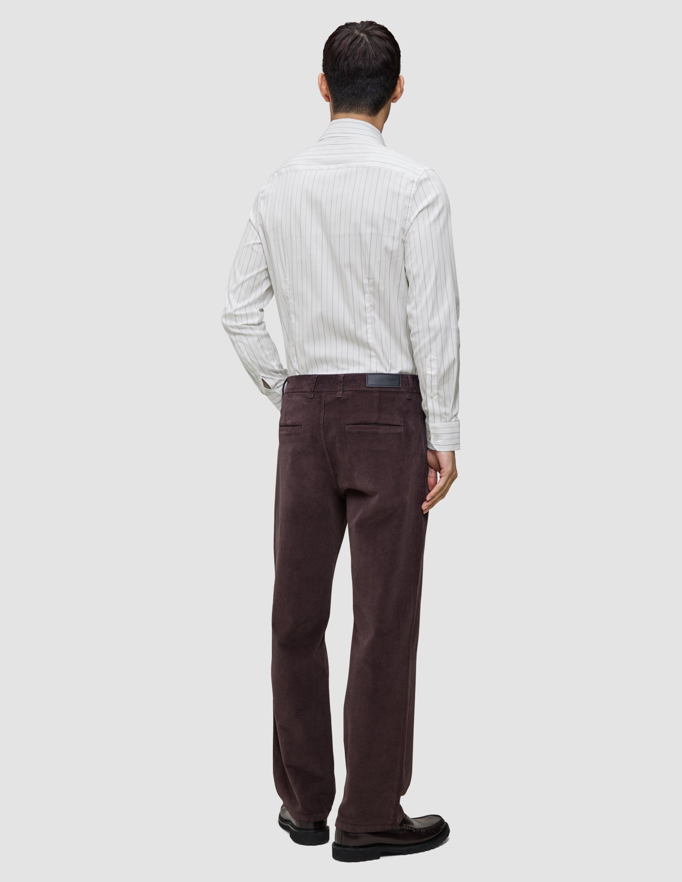Bagfra-billede af en person iført en Elevated Shirt Slim i lysegrå striber og mørkebrune bukser.